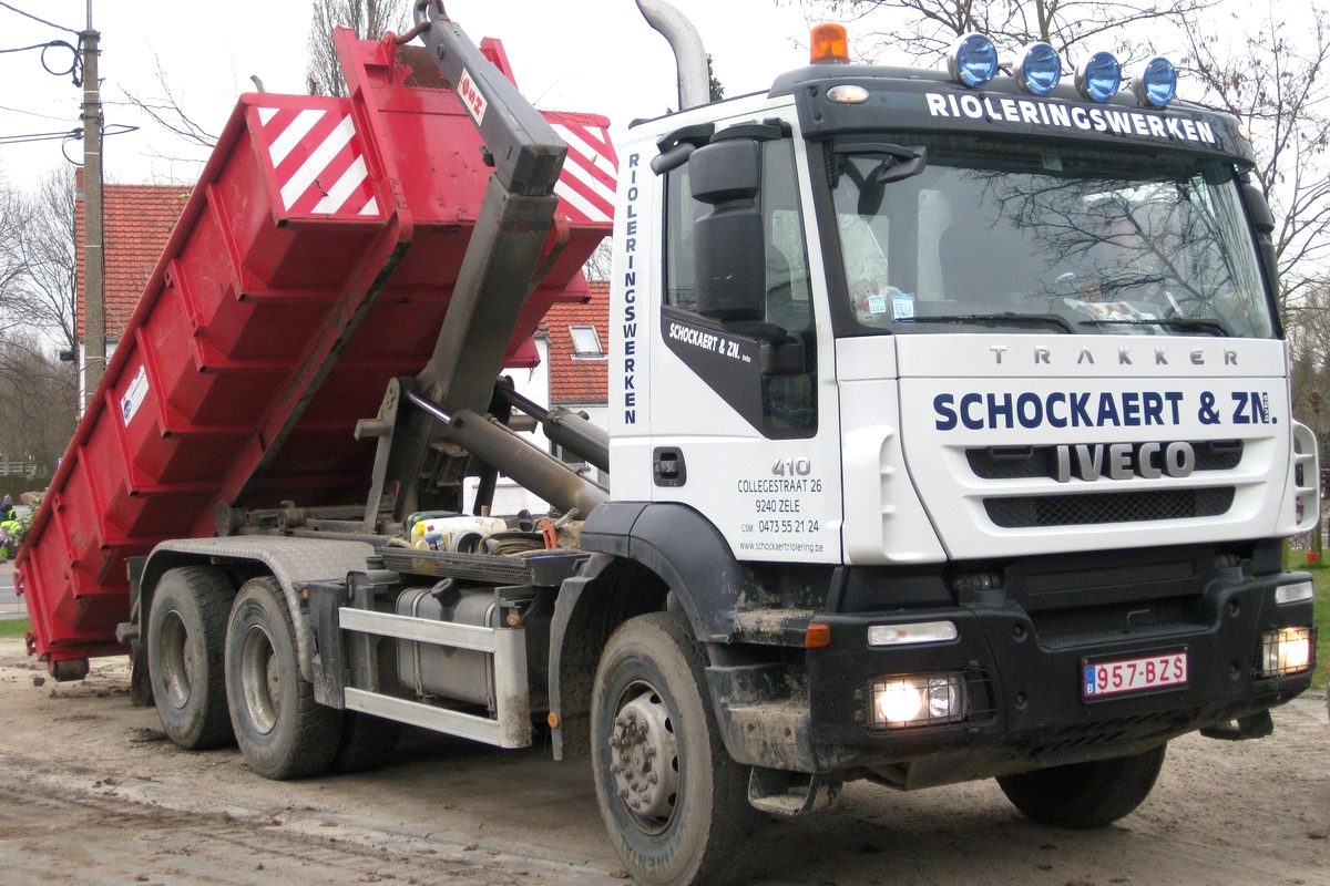 Witte Iveco Trakker met kraan van Schockaert en Zn. die een rode afzetcontainer plaatst.