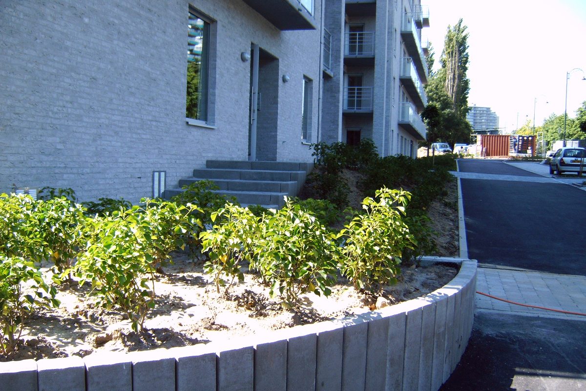 Afgewerkte omgevingsaanleg bij een appartementsgebouw met plantvak in betonnen palissade, gekasseide strook en blauwstenen treden.